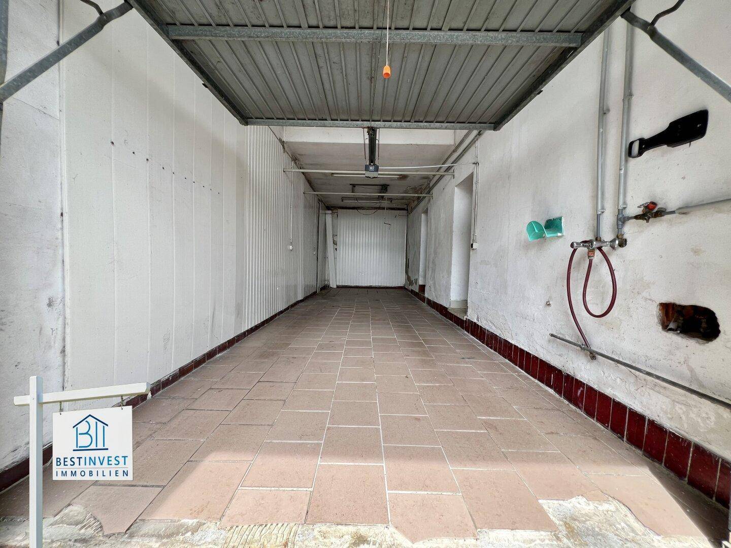 Lange Garage mit Fliesenboden und Rolltor, bietet Platz für mehrere Fahrzeuge.