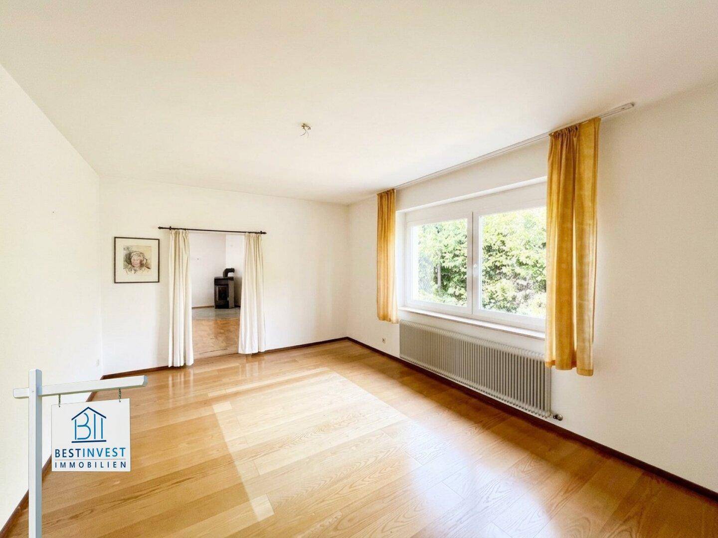 Helles Zimmer mit Parkettboden und großen Fenstern, verbunden mit einem weiteren Raum.