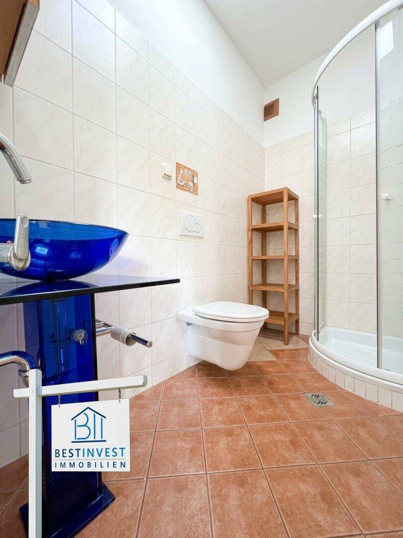 Modernes Badezimmer mit blauer Waschschale, Dusche und Wand-WC.