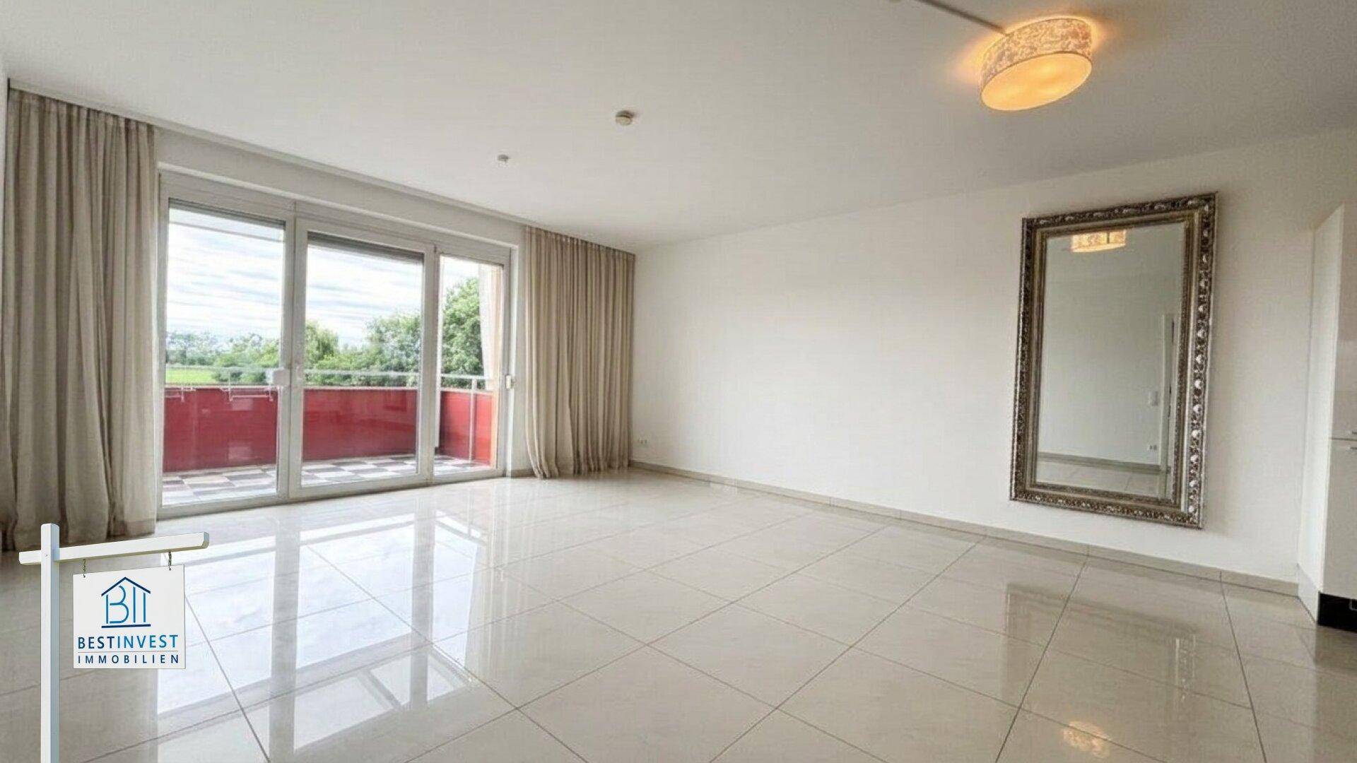 Helles, leeres Wohnzimmer mit großen Fliesen und Zugang zu einem Balkon mit weitem Blick.