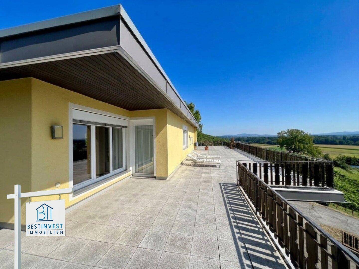 Große geflieste Terrasse mit Liegestühlen und weitem Blick über die Landschaft.