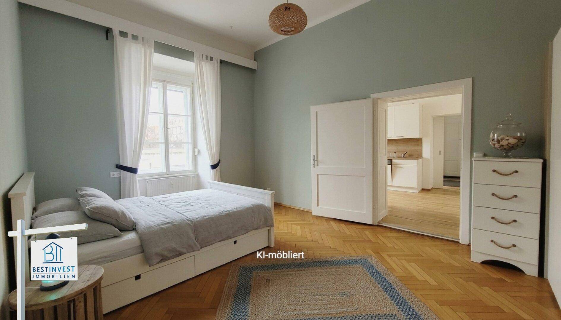 Helles Schlafzimmer mit Fischgrätparkett und Zugang zu einer kleinen Küchenzeile.