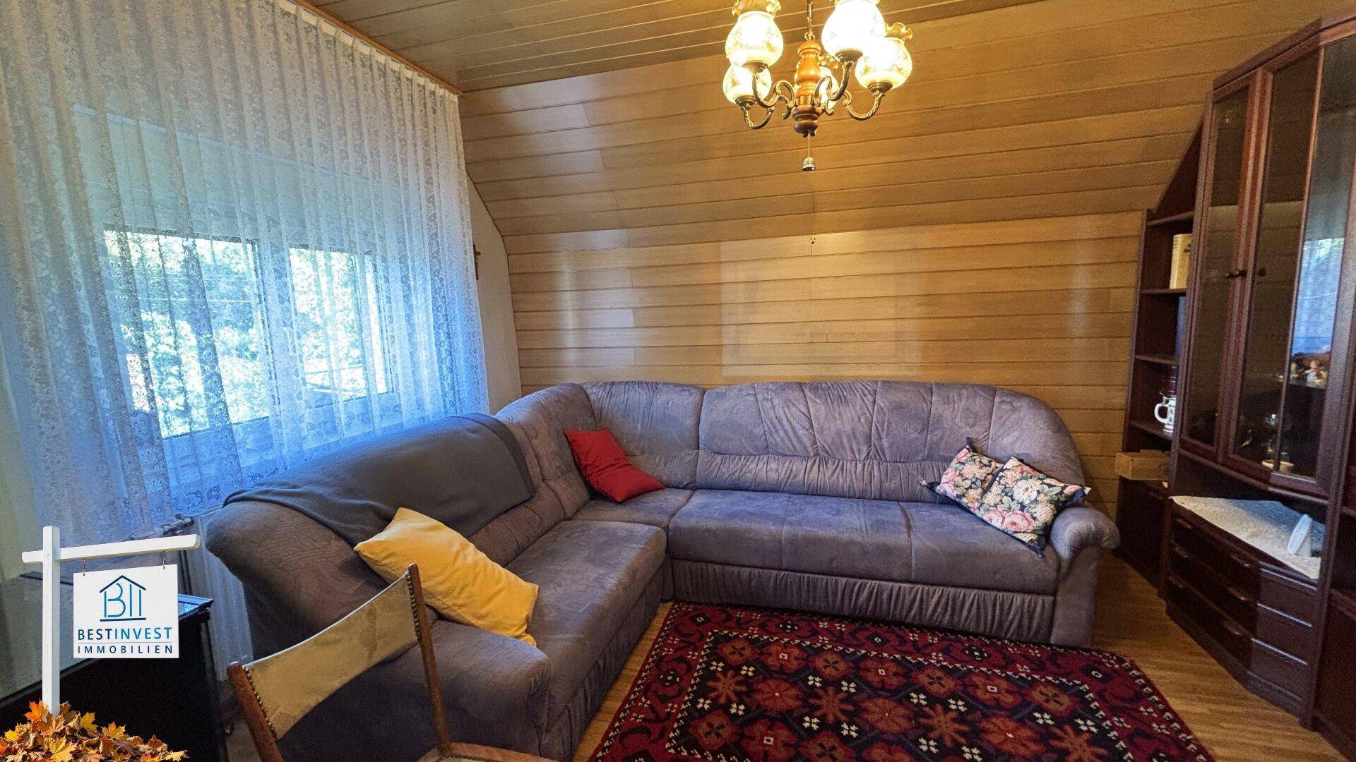 Dachgeschoss-Wohnzimmer mit Holzvertäfelung, gemütlichem Sofa und schrägen Wänden.