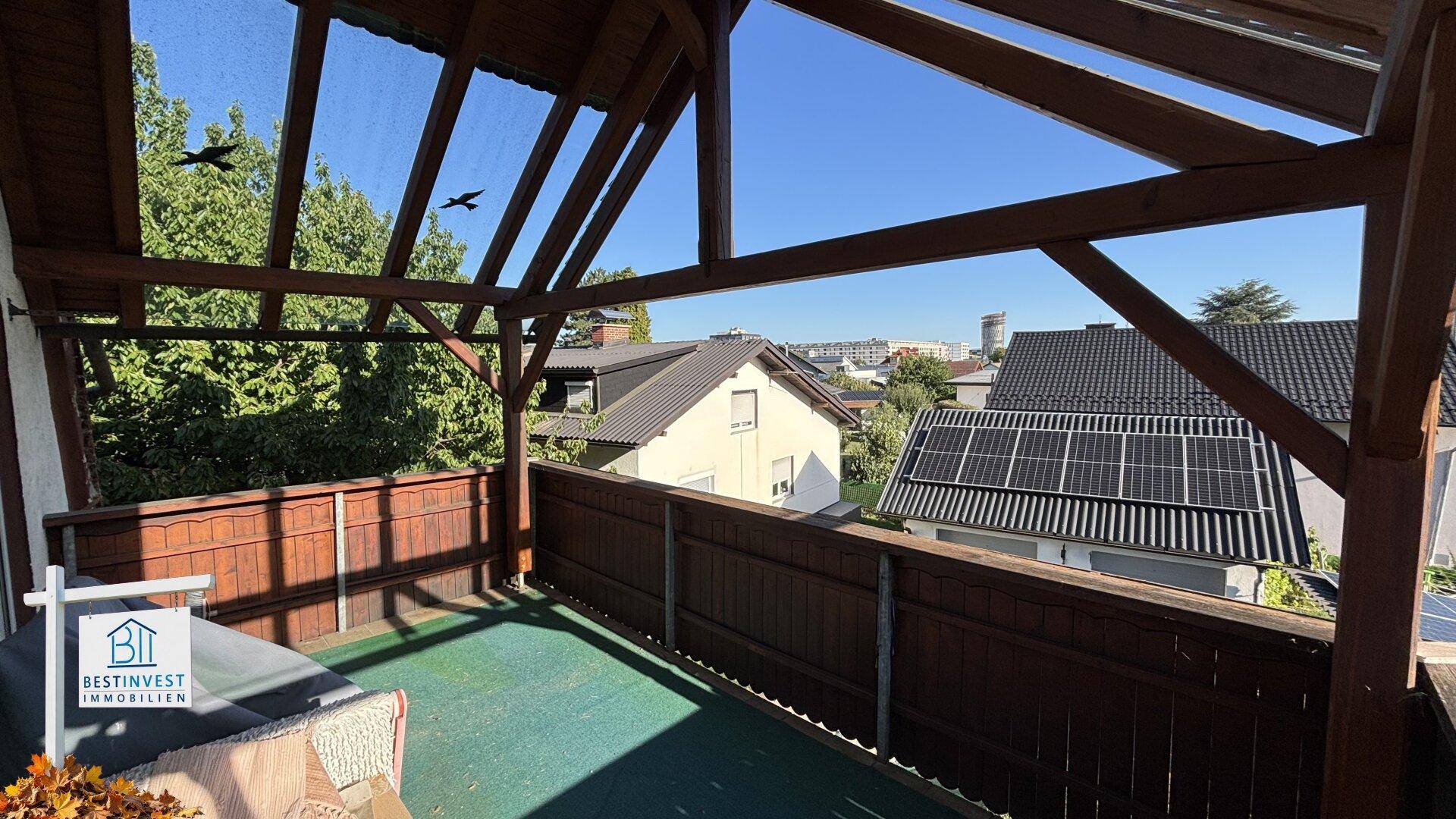 Überdachte Terrasse mit Holzpergola und Blick auf benachbarte Häuser mit Solaranlage.