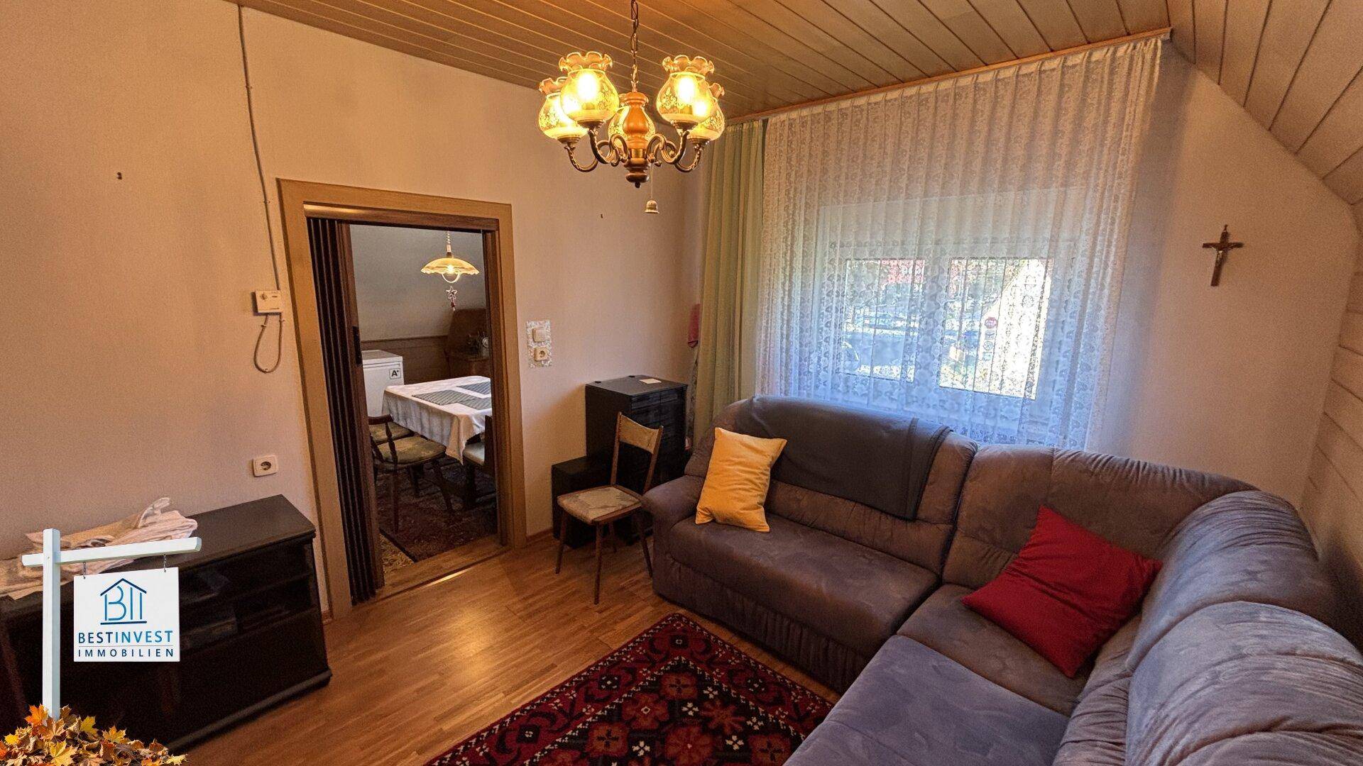 Helles Dachgeschoss-Wohnzimmer mit Holzvertäfelung, Sofa und Zugang zum Essbereich.