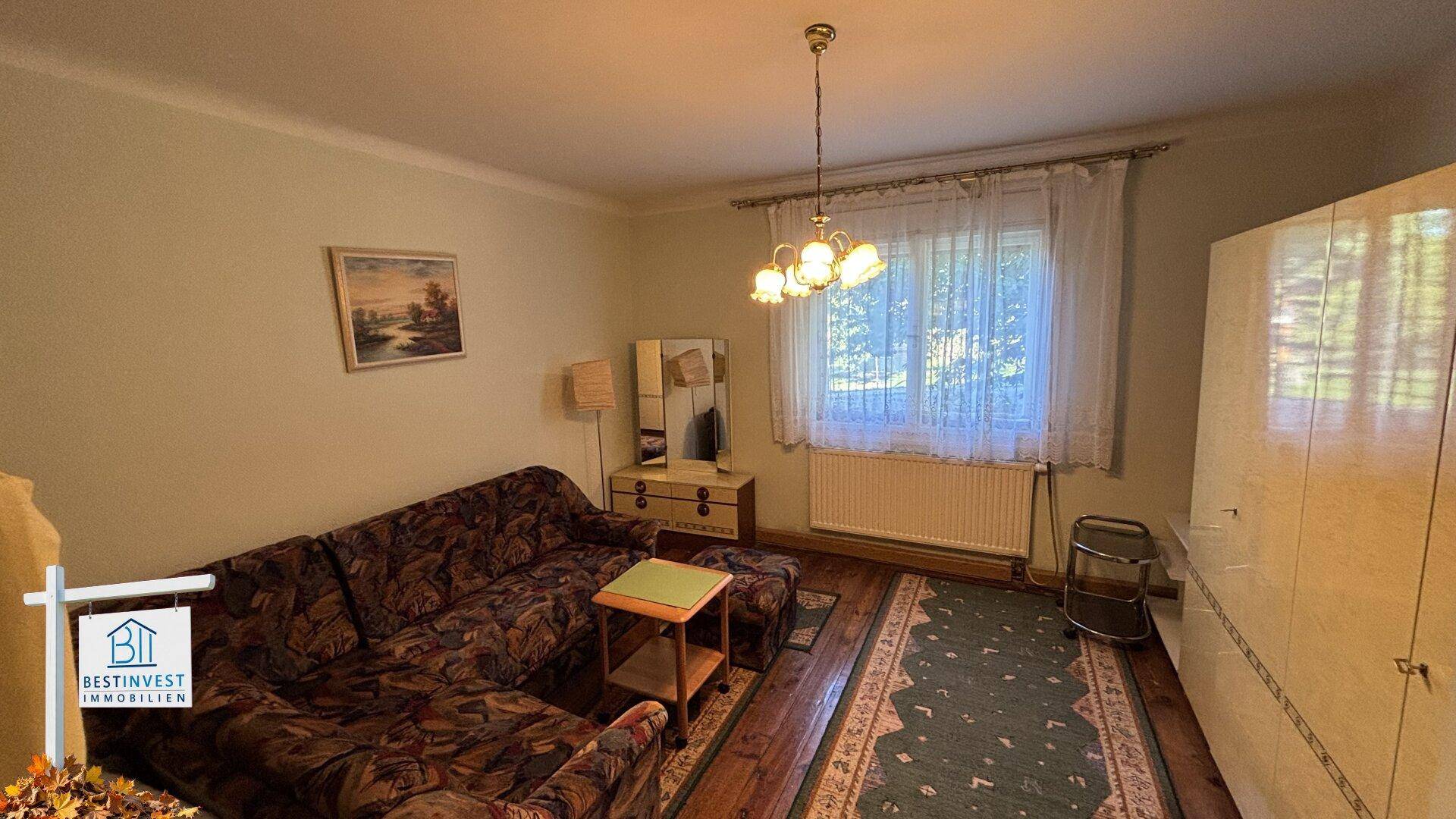 Gemütliches Wohnzimmer mit traditionellem Sofa, Teppich und Blick in den Garten.