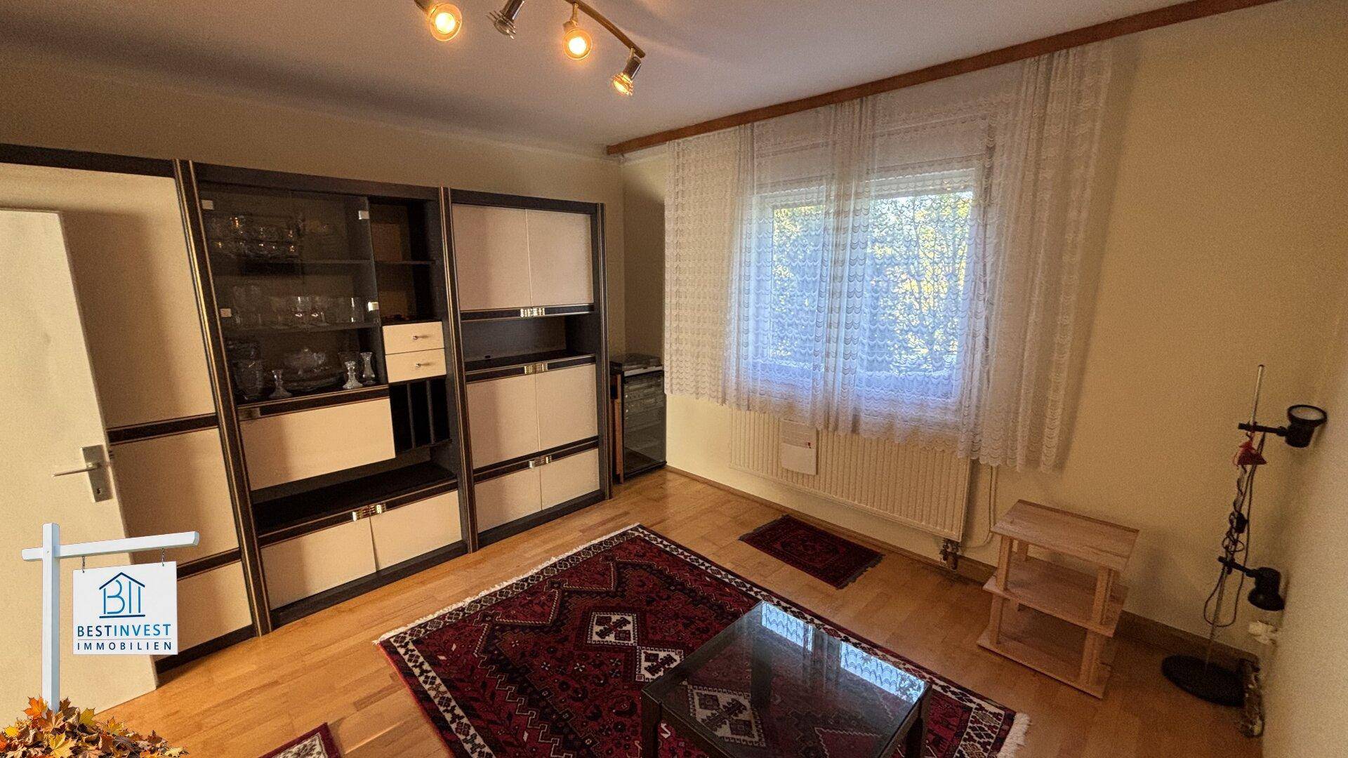 Wohnzimmer mit Holzboden, großem Schrank und Fenster, das viel Licht hereinlässt.