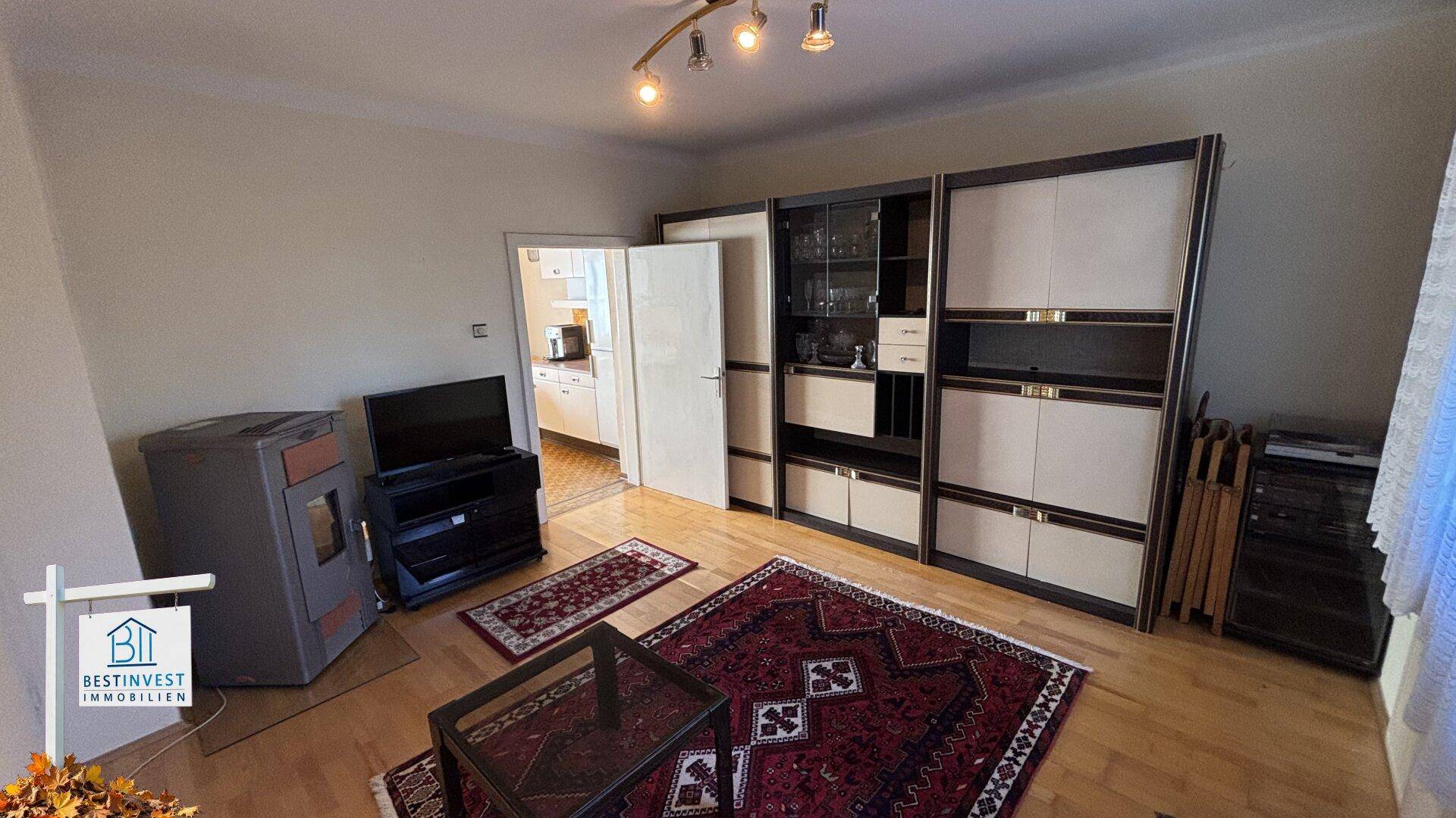 Geräumiges Wohnzimmer mit Holzboden, Kaminofen und Zugang zur Küche.