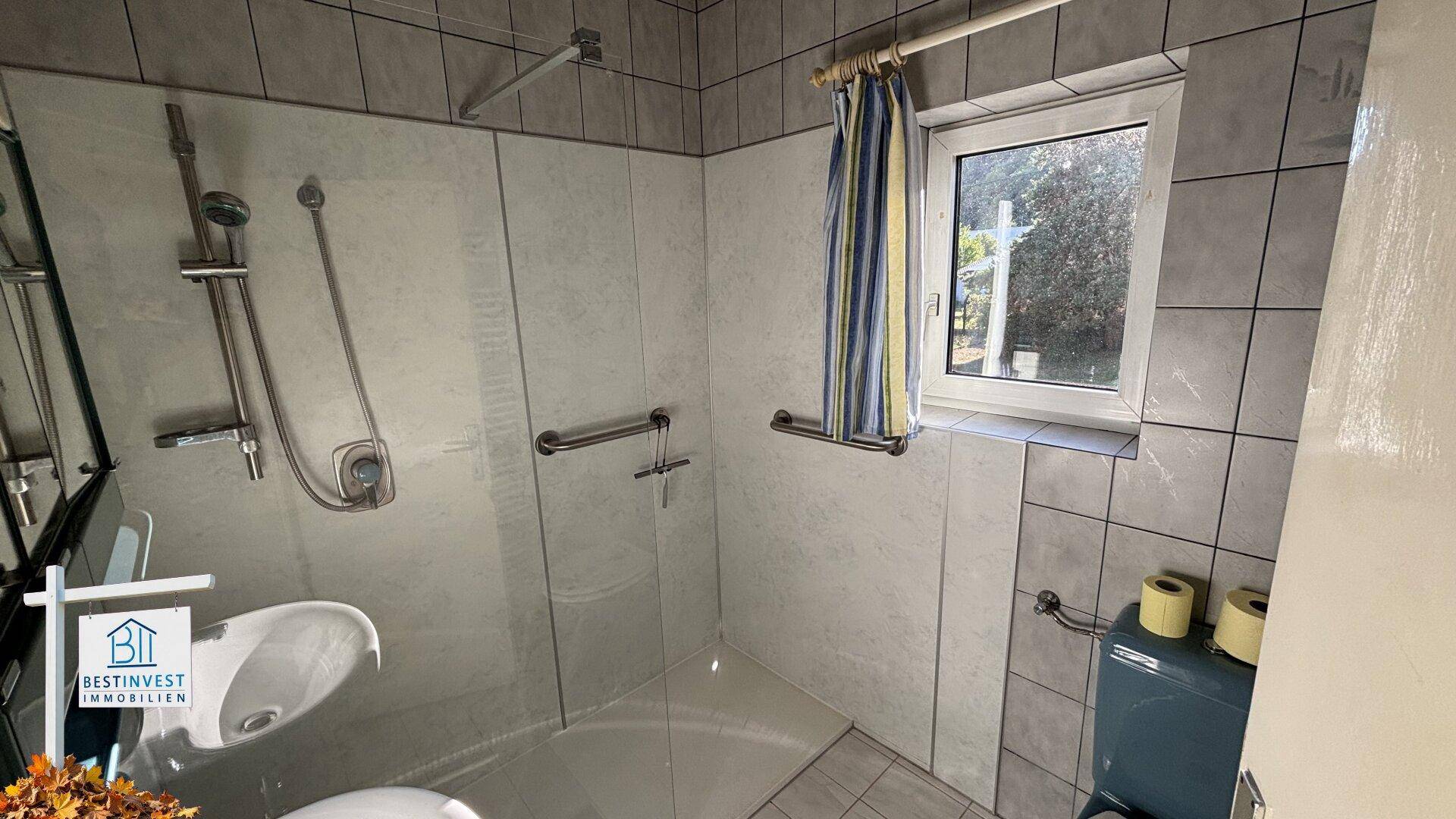 Badezimmer mit Dusche, Fenster und Haltegriffen für zusätzliche Sicherheit.