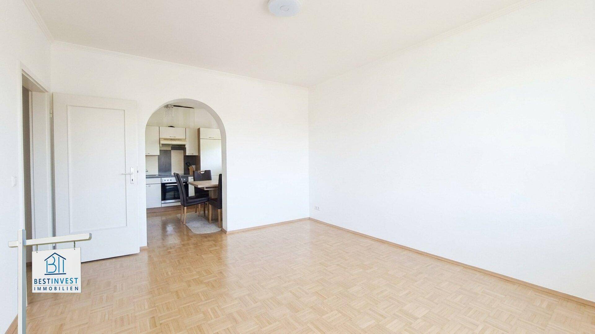 Helles Wohnzimmer mit Parkettboden und offenem Durchgang zur angrenzenden Küche.