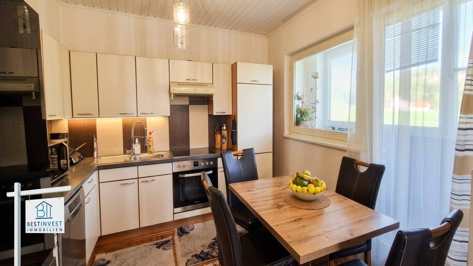 Helle Einbauküche mit Essbereich, Holzdecke und Blick ins Grüne durch das Fenster.