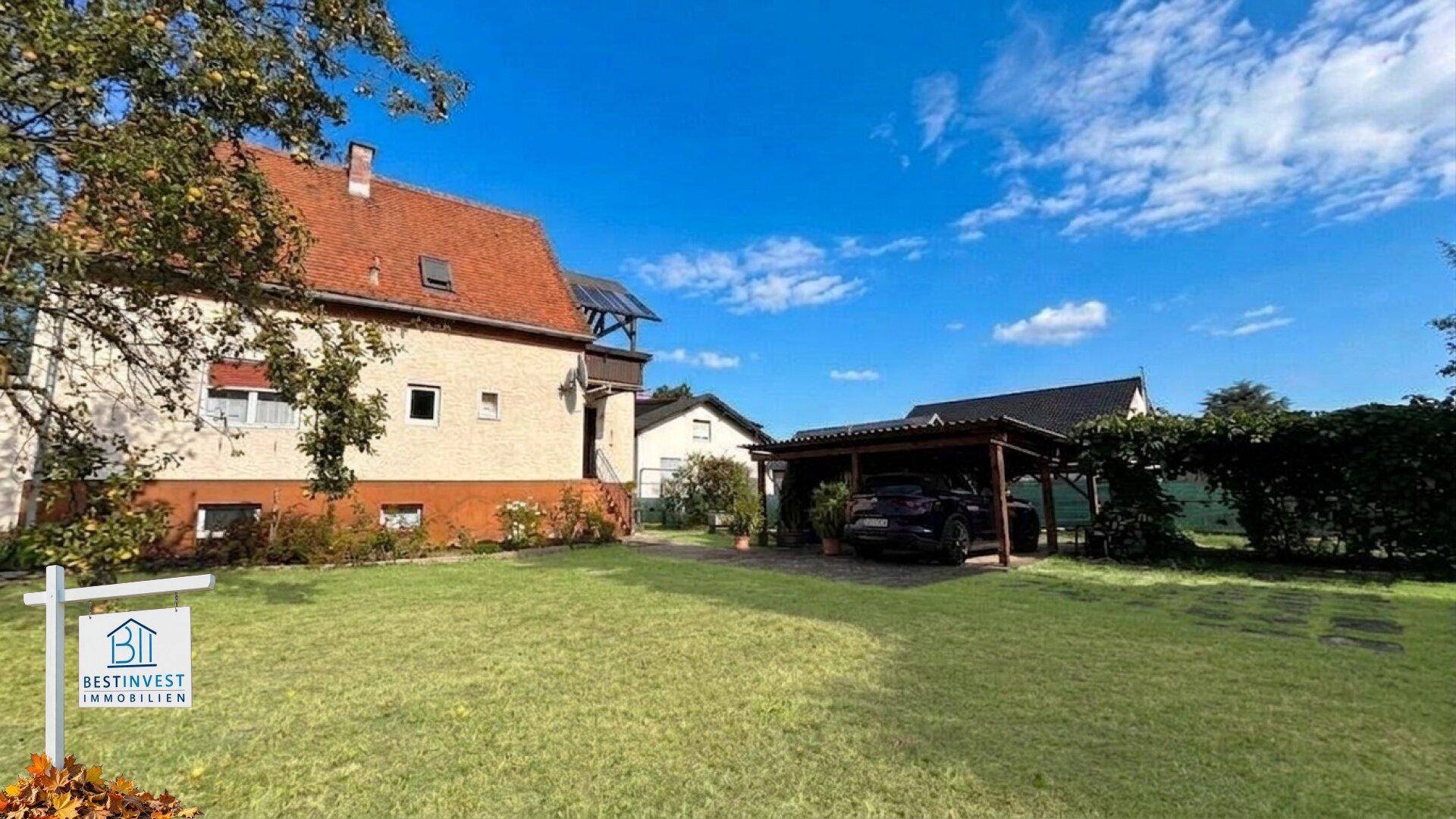 Großzügiger Gartenbereich mit Rasenfläche, Baumbestand und einem Carport für Fahrzeuge.