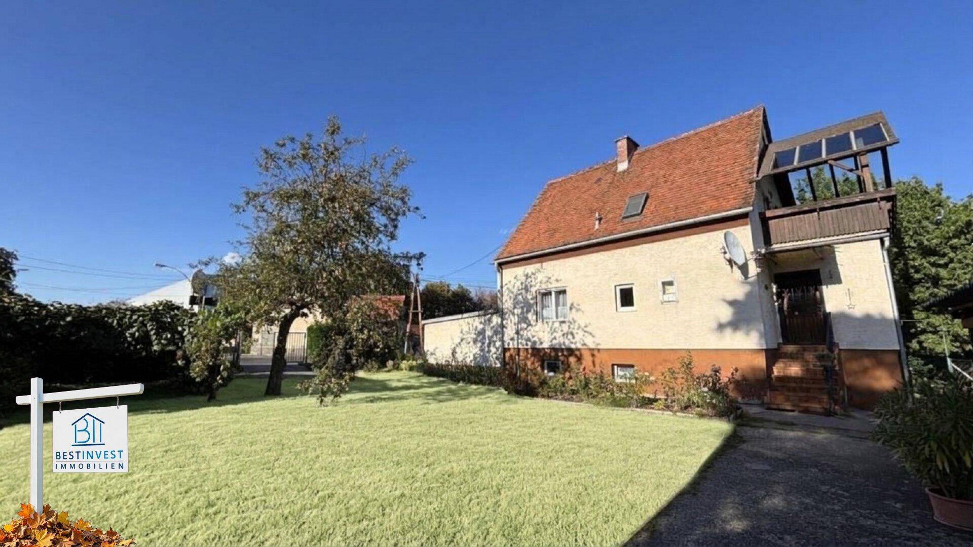 Gepflegter Garten mit Rasenfläche und einem älteren Einfamilienhaus unter blauem Himmel.