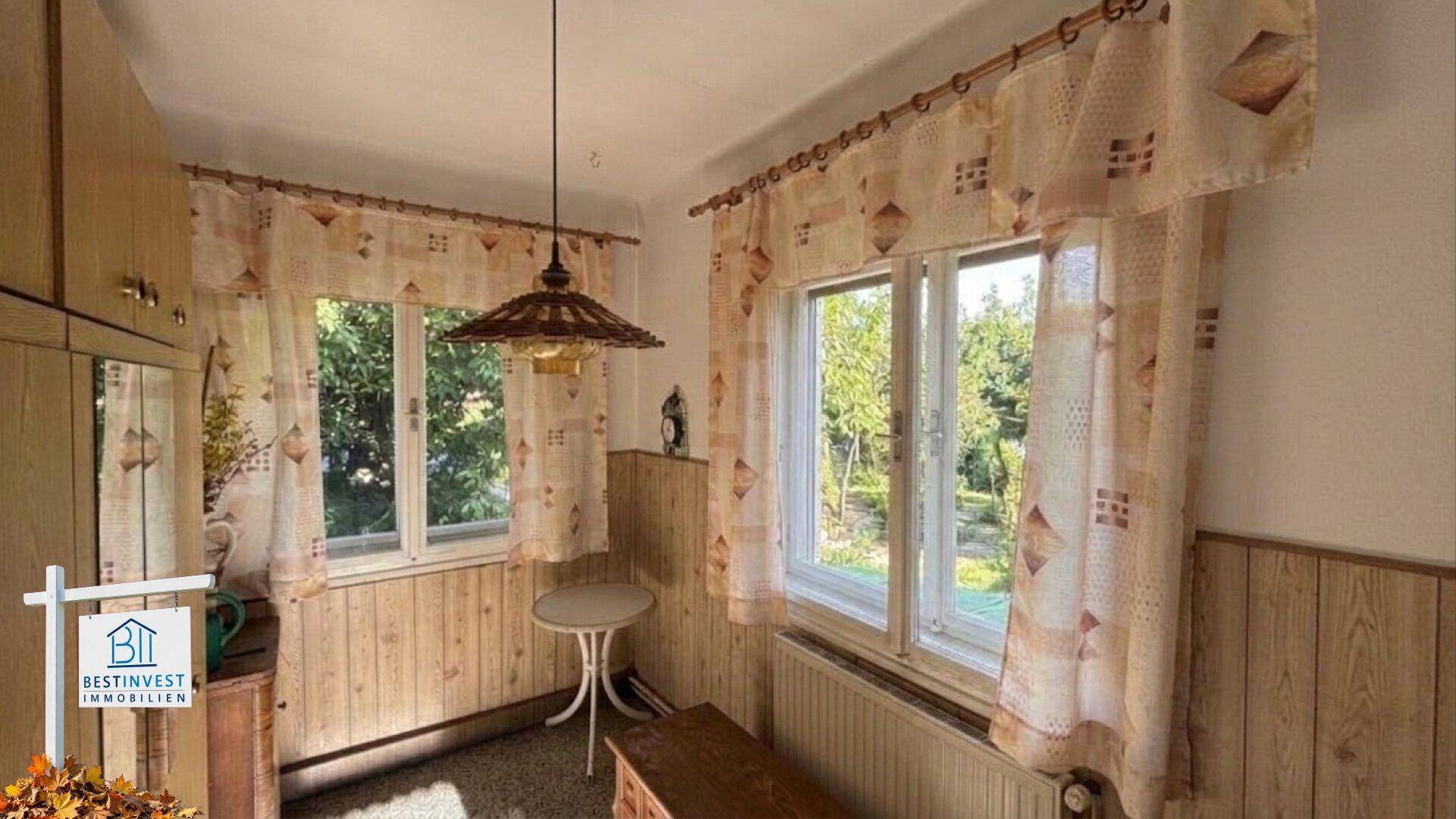 Kleiner Raum mit Holzvertäfelung, zwei Fenstern und Blick ins Grüne.