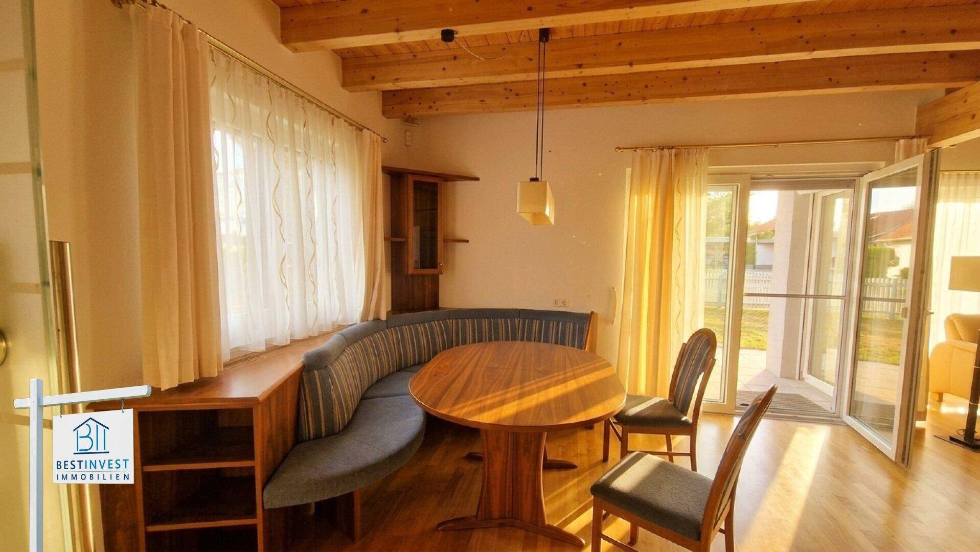 Heller Essbereich mit Eckbank, Holzbalkendecke und Zugang zu einem Außenbereich.