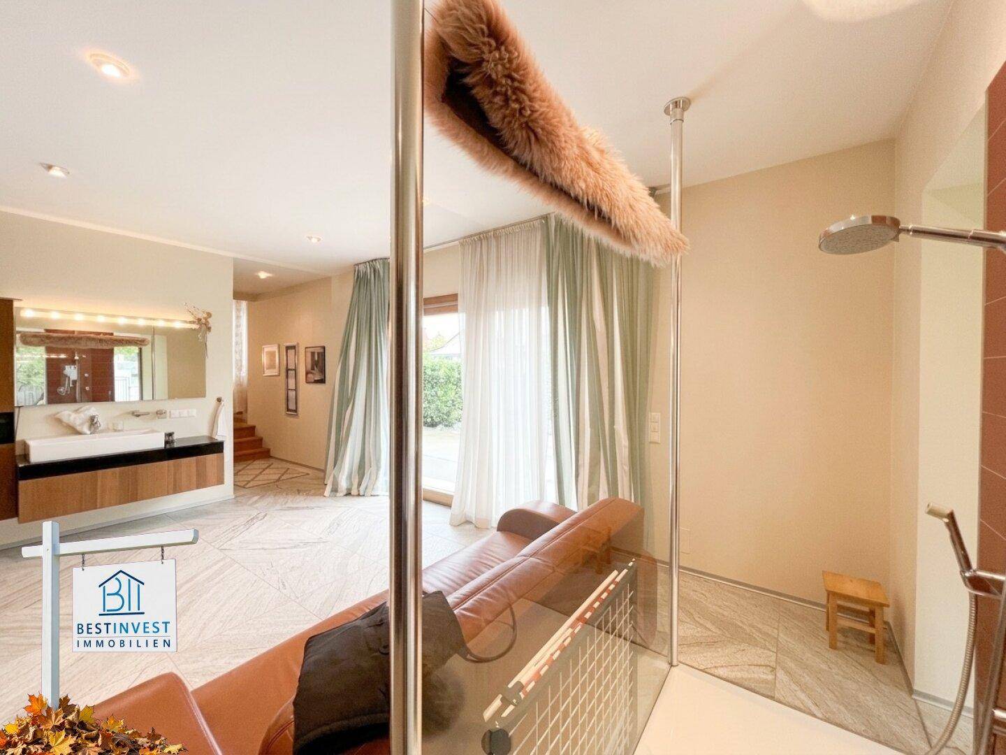 Offener Wellnessbereich mit rotem Sofa, Dusche und Waschtisch im Hintergrund.