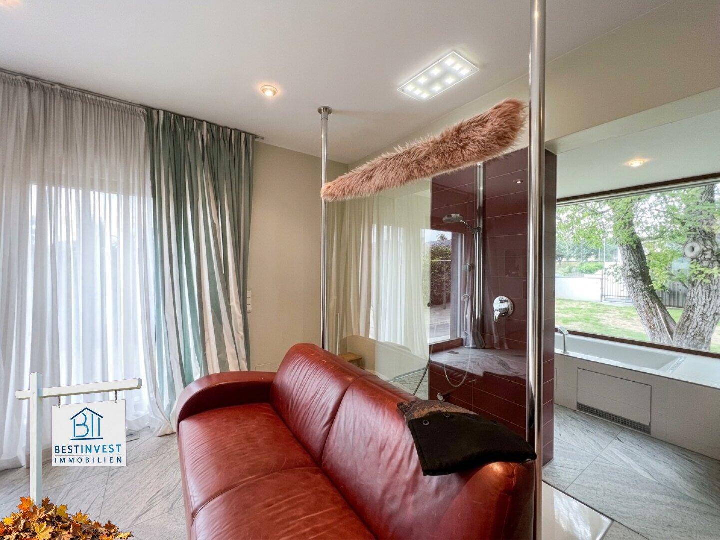 Wellnessbereich mit rotem Sofa, Dusche und Whirlpool, durch Glaswände getrennt.