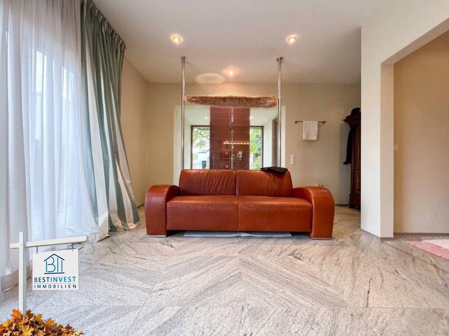 Großzügiger Wellnessbereich mit rotem Ledersofa und elegantem Steinboden.