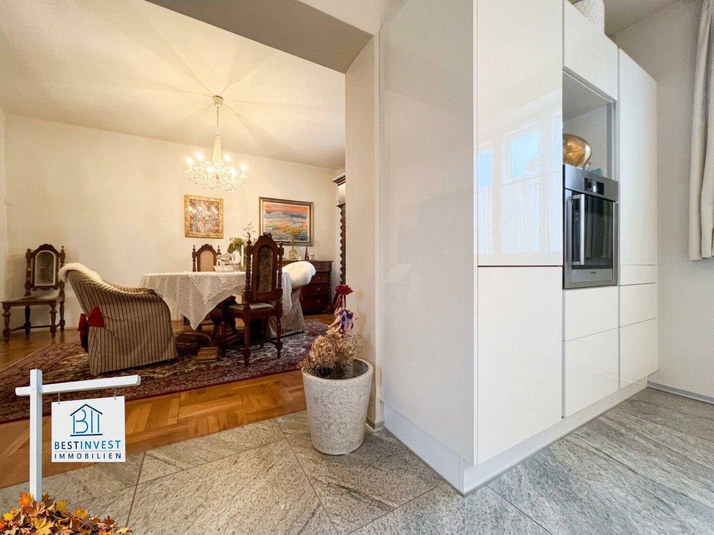 Moderne weiße Küche mit Hochglanzfronten, offen zum eleganten Esszimmer mit Kronleuchter.