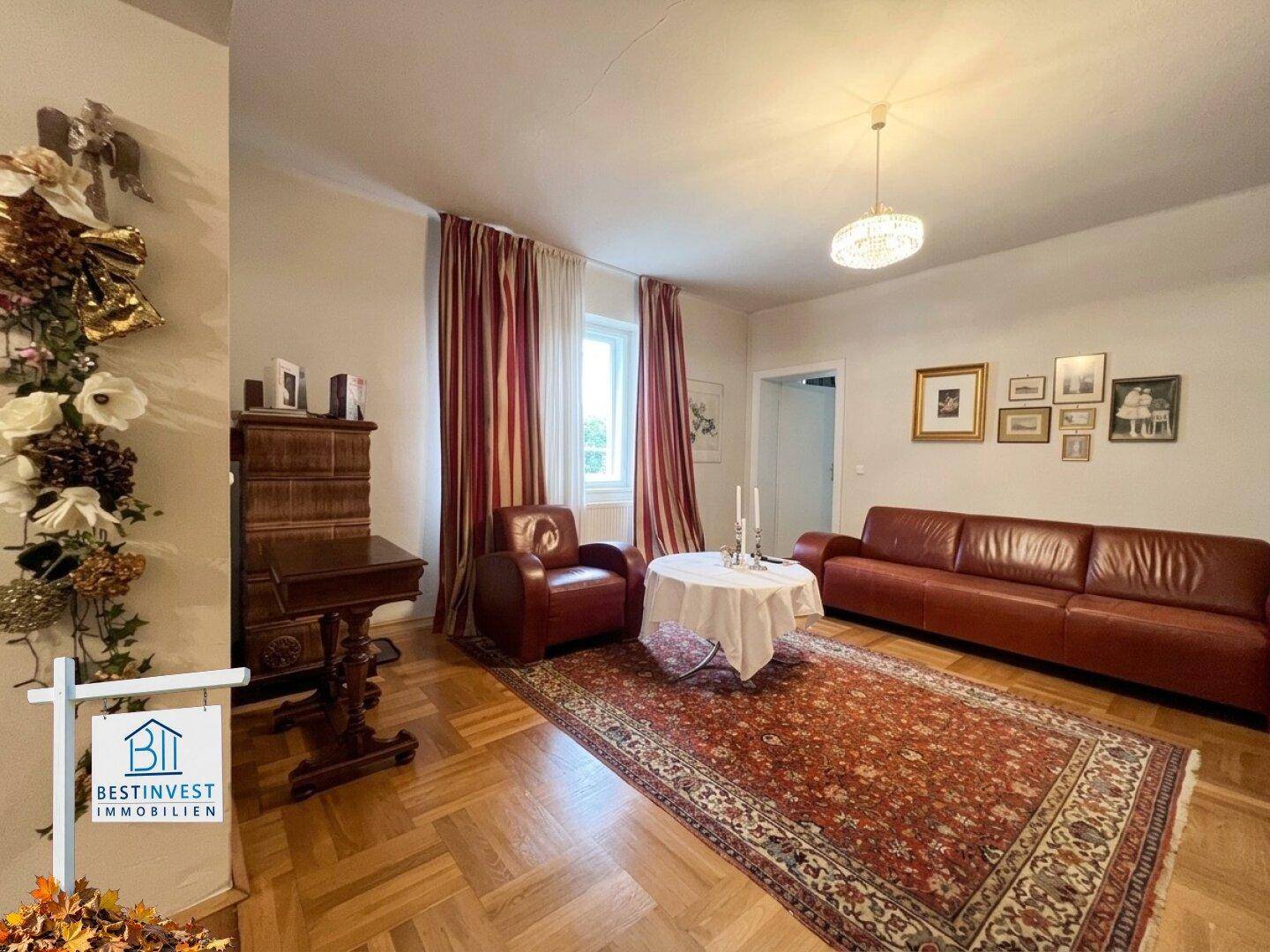 Gemütliches Wohnzimmer mit rotem Ledersofa, Sessel und klassischem Fischgrätparkett.
