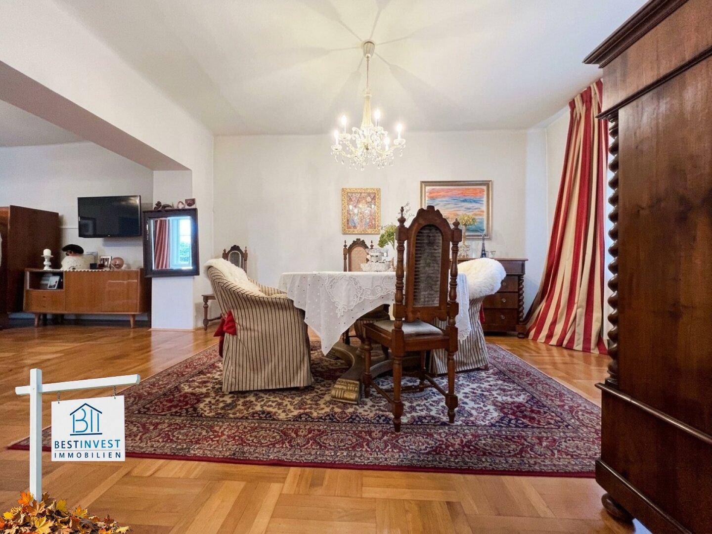 Geräumiges Esszimmer mit Kronleuchter, klassischen Möbeln und offenem Übergang zum Wohnbereich.