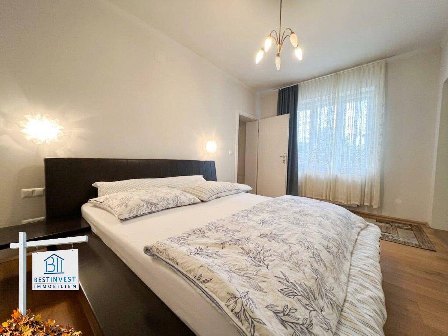 Gemütliches Schlafzimmer mit Doppelbett, Holzboden und Vorhängen am Fenster.