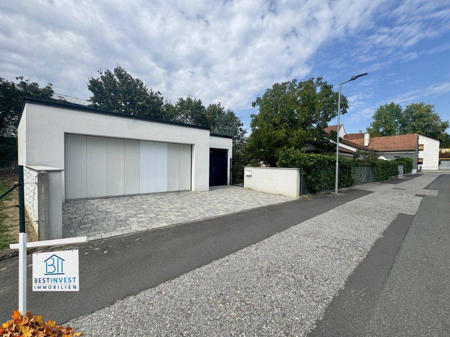 Moderne Garage mit gepflasterter Einfahrt und Zugang zum Grundstück unter bewölktem Himmel.