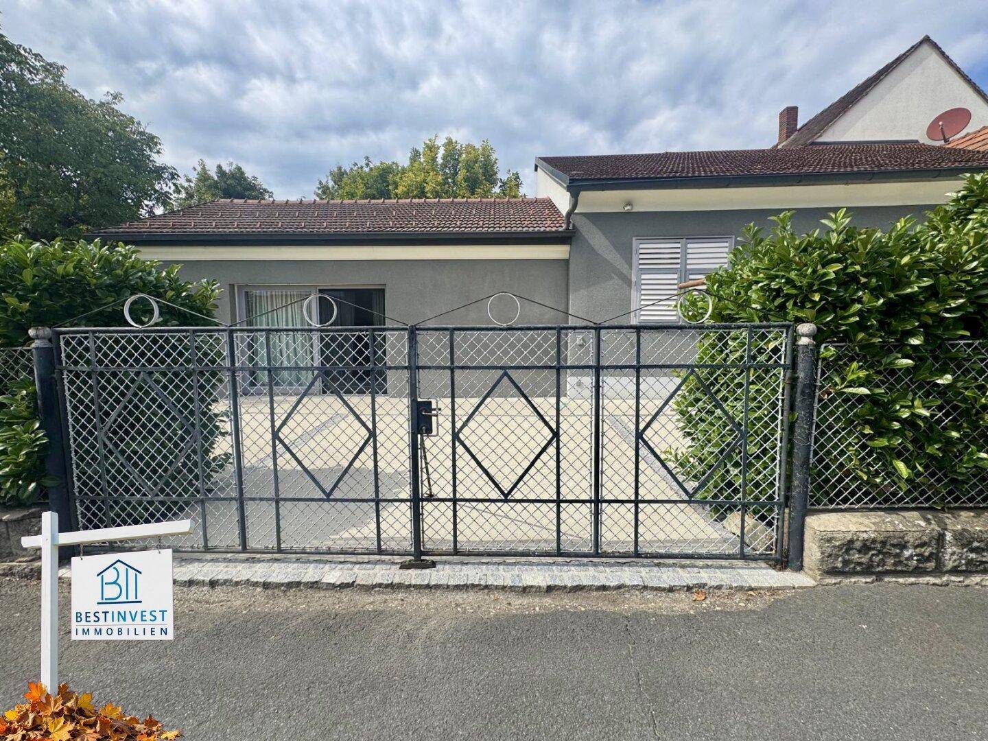 Vorderansicht des Hauses mit schmiedeeisernem Tor, gepflegter Hecke und grauer Fassade.
