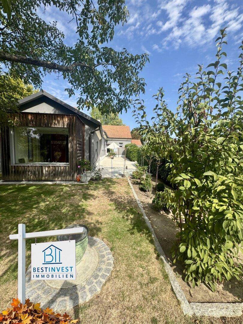 Idyllischer Gartenbereich mit gepflegtem Rasen, Bäumen und einem charmanten Haus im Hintergrund.