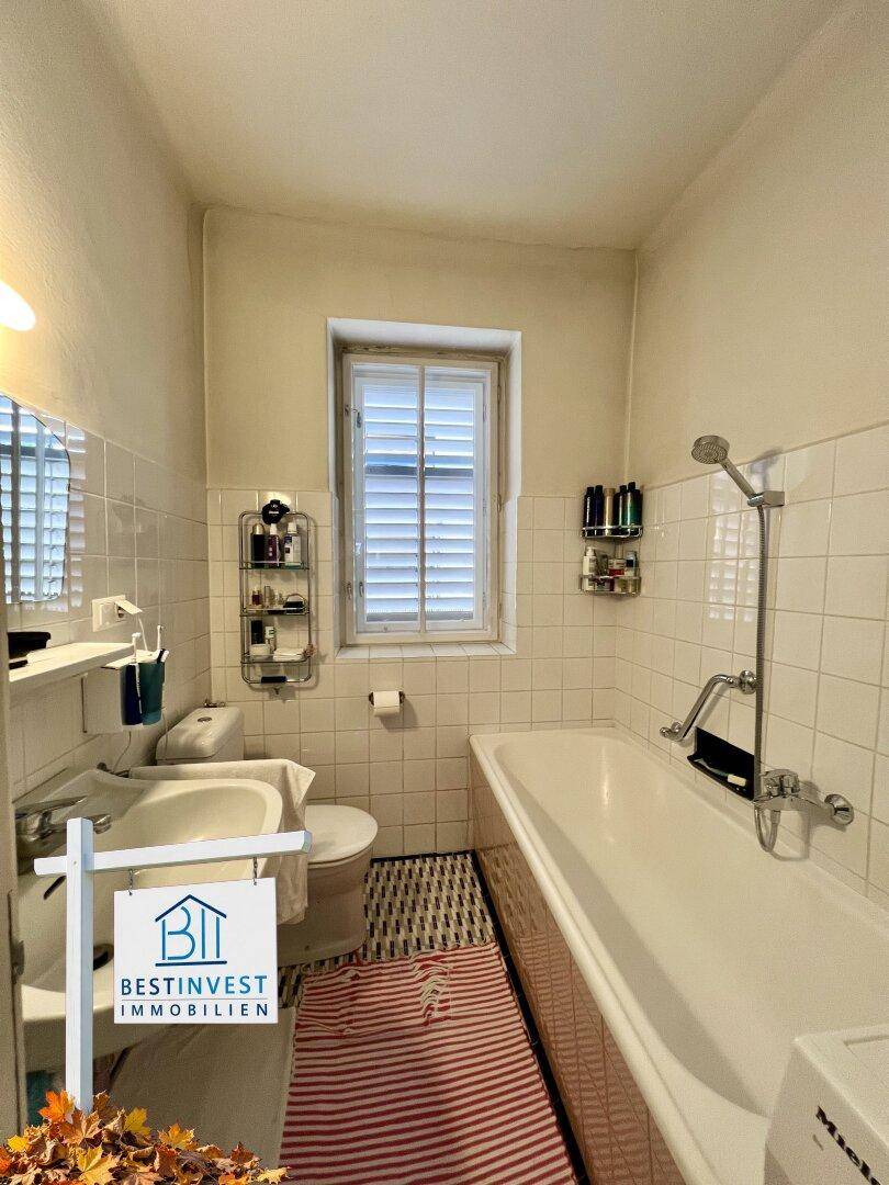 Klassisches Badezimmer mit Badewanne, Toilette, Waschbecken und Fenster, hell gefliest.