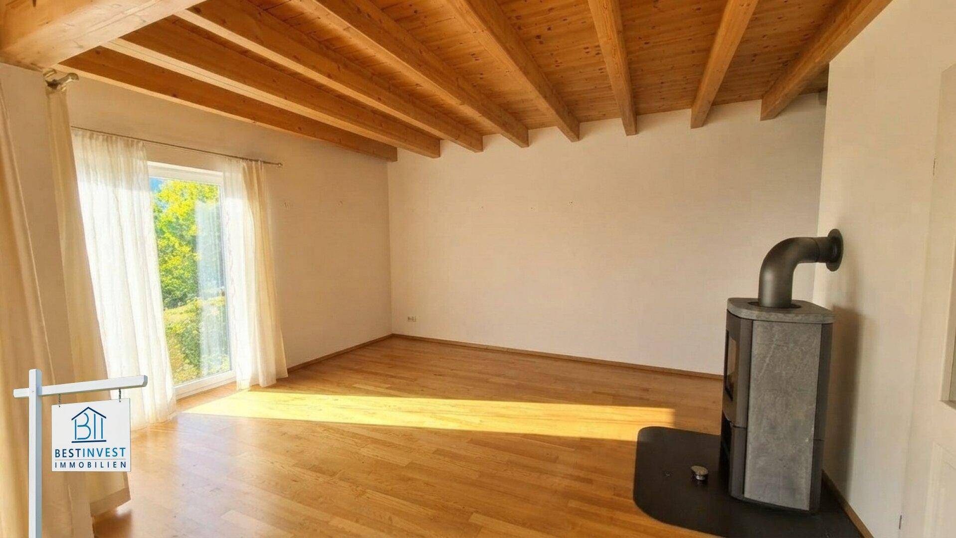 Geräumiges Wohnzimmer mit Holzbalkendecke, Parkettboden und einem modernen Holzofen.
