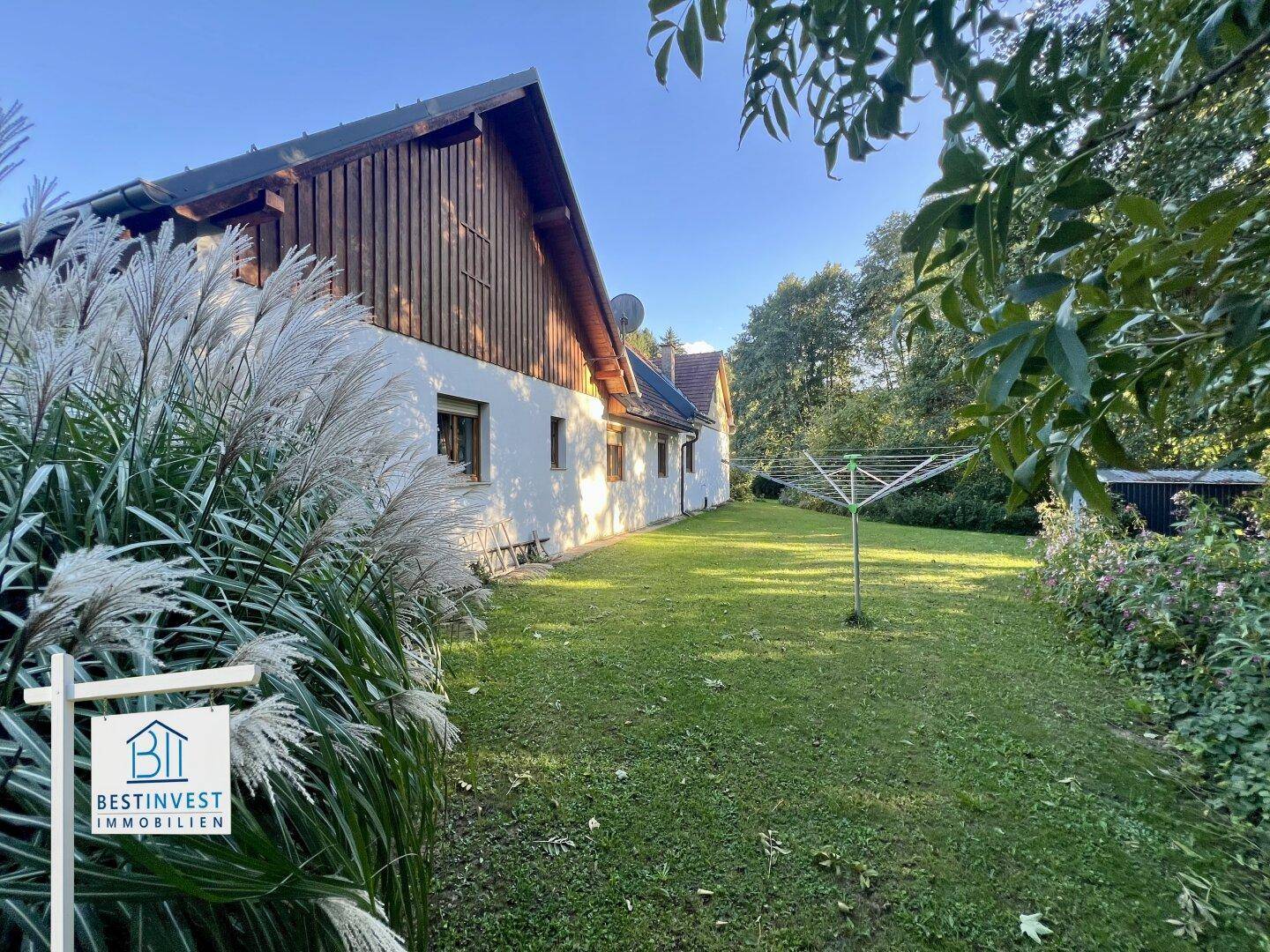 Weitläufiger Rasenbereich neben dem Haus mit Wäschespinne und umgebender Natur.