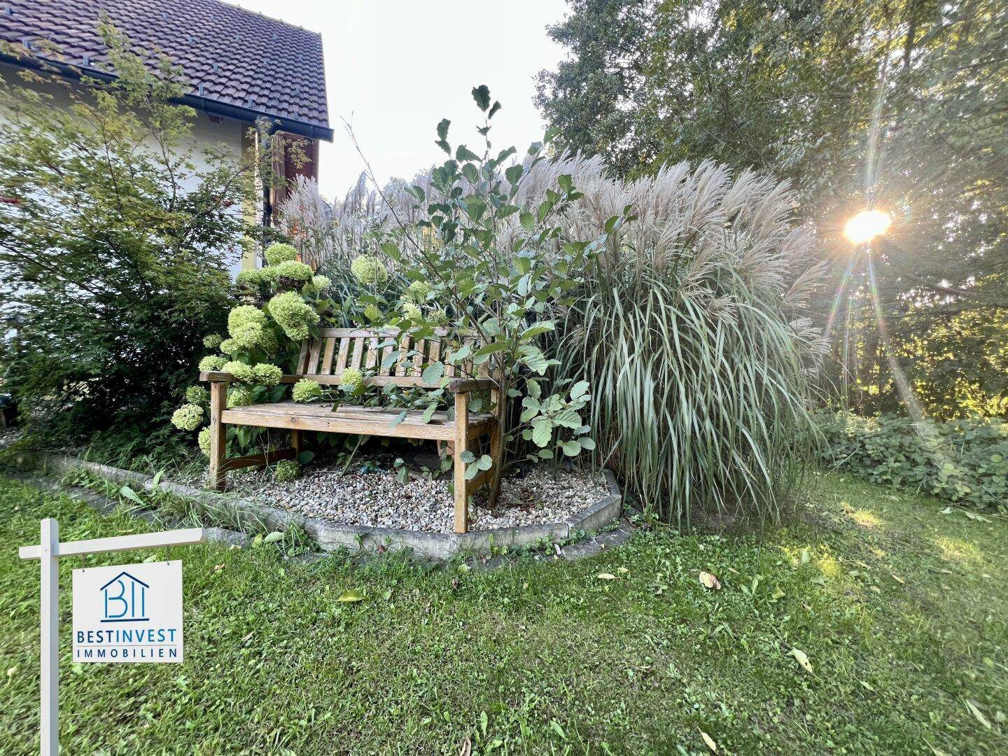Rustikale Holzbank in einem Blumenbeet, umgeben von hohen Gräsern und Pflanzen im Garten.