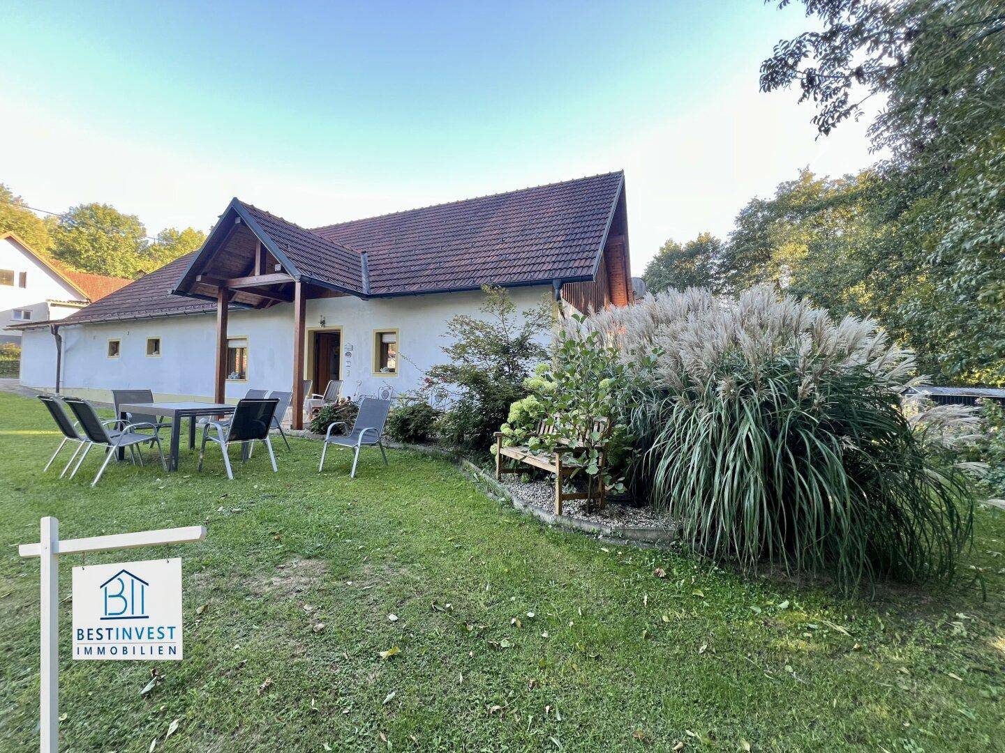 Idyllischer Gartenbereich mit Esstisch und Stühlen, umgeben von üppigem Grün und einem charmanten Haus.