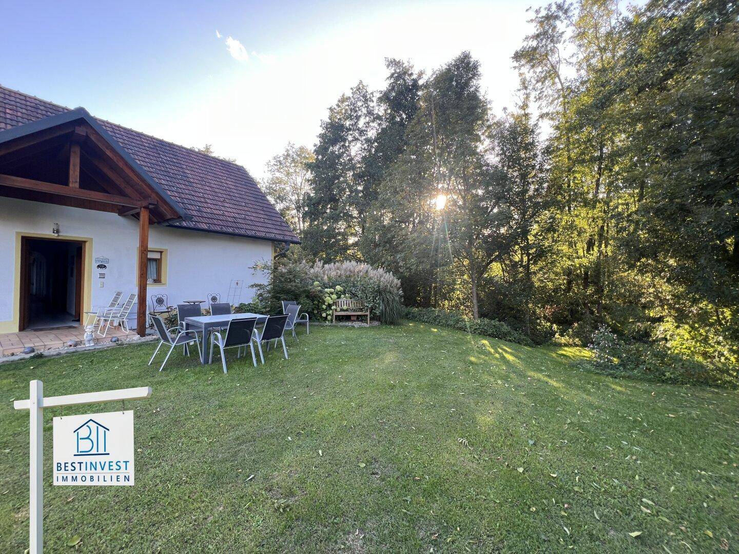 Gemütlicher Garten mit Esstisch und Stühlen, umgeben von üppiger Vegetation und sonnigem Ambiente.