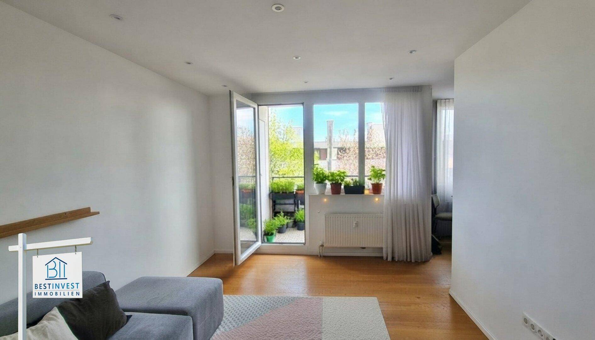 Heller Wohnbereich mit Holzboden, modernem Sofa und Zugang zu einem bepflanzten Außenbereich.