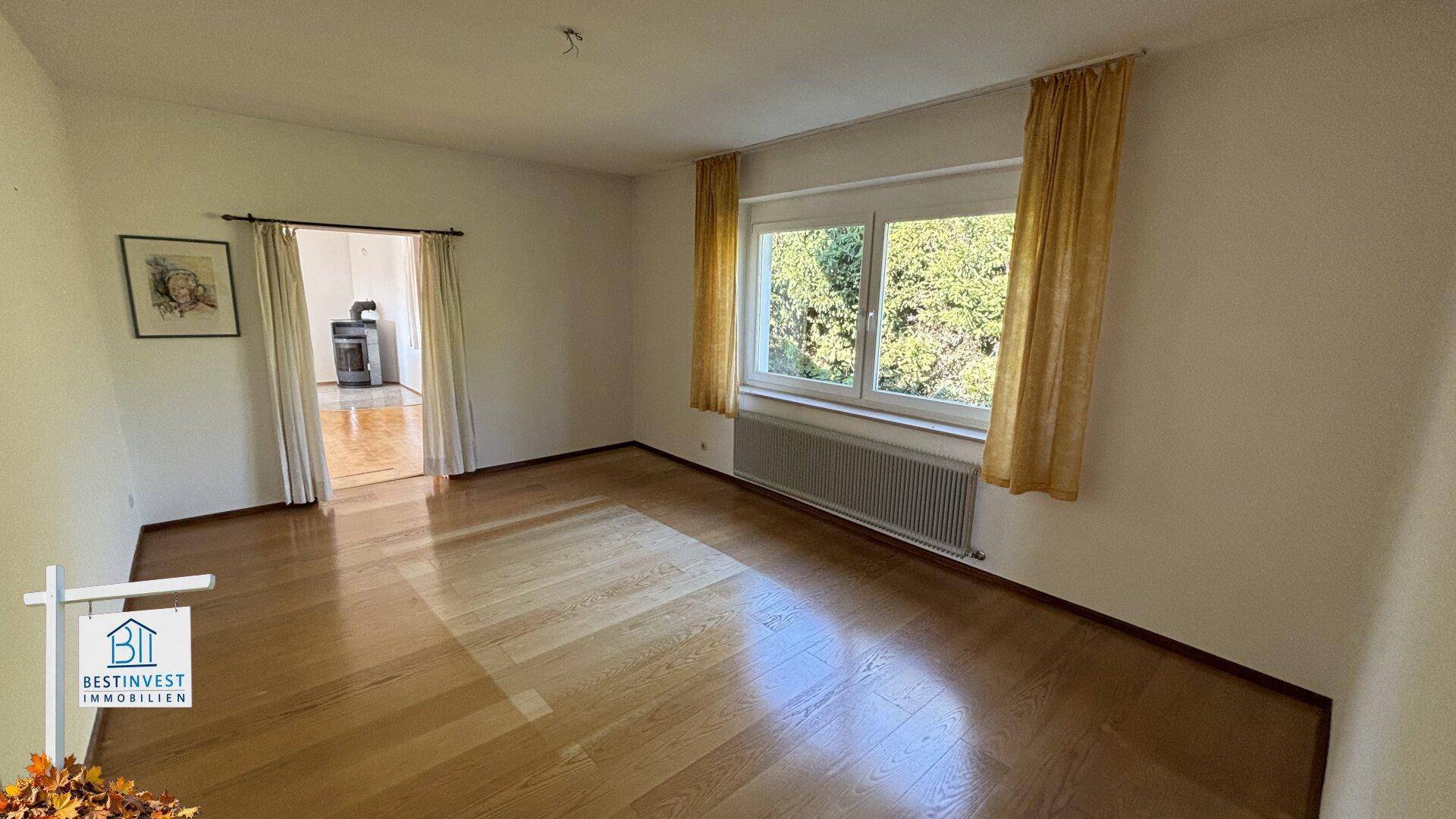 Leeres Zimmer mit Parkettboden und Fenster, das zu einem weiteren Raum führt.