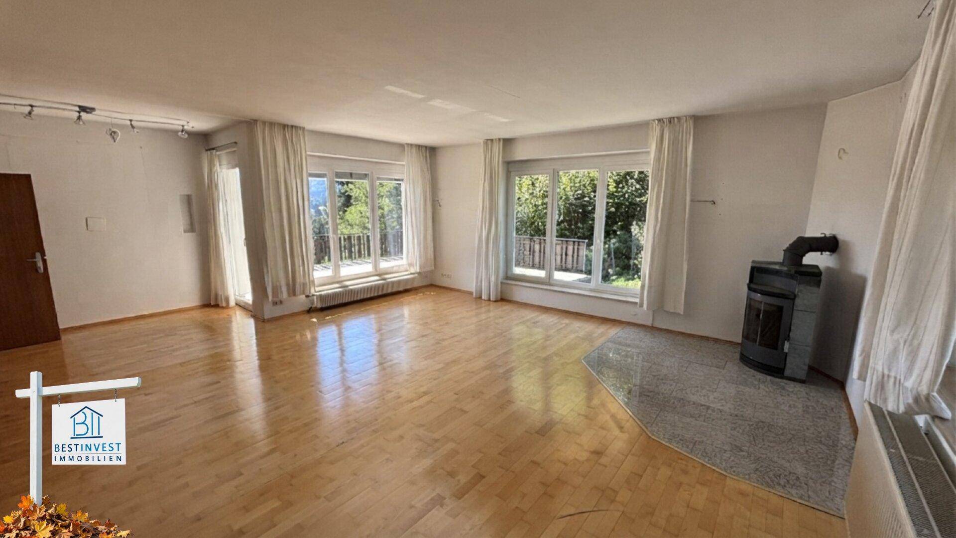 Helles Wohnzimmer mit Parkettboden, Kaminofen und großen Fenstern mit Ausblick.
