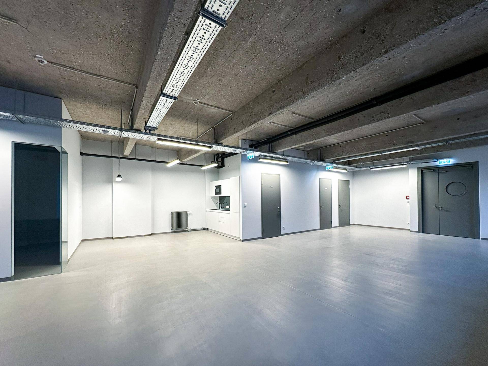 Großer, leerer Bürobereich mit mehreren Türen, hohen Decken und einem funktionalen Tresenbereich, ideal für flexible Nutzung.