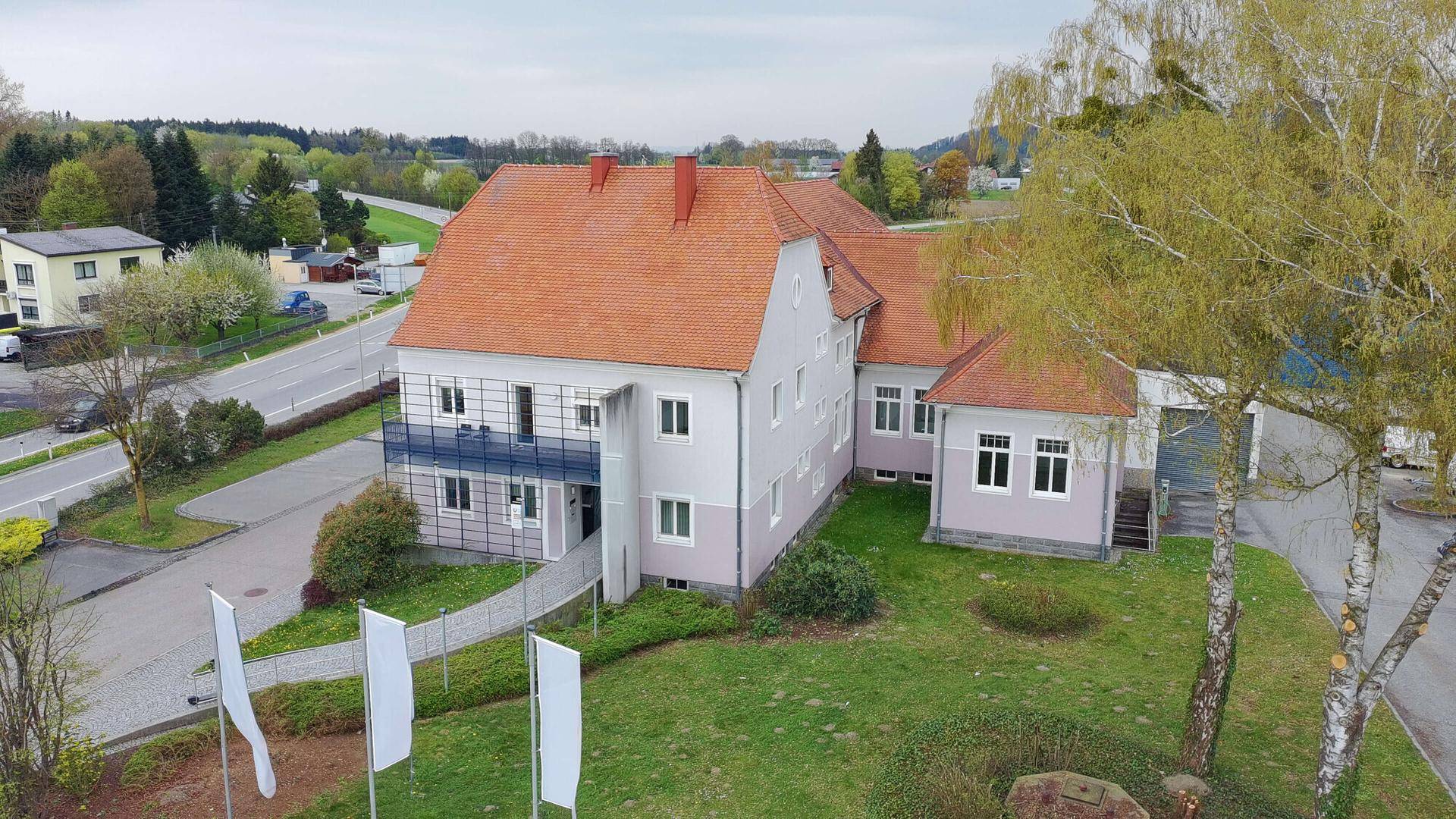 Bürogebäude mit traditionellem roten Ziegeldach, Balkon und gepflegter Grünanlage im Vordergrund.