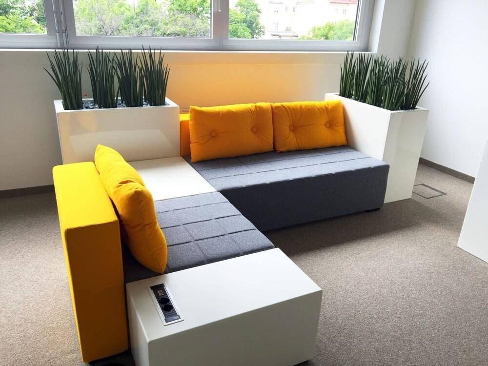 Detailansicht eines modernen Loungebereichs mit gelben Kissen und integrierten Steckdosen.