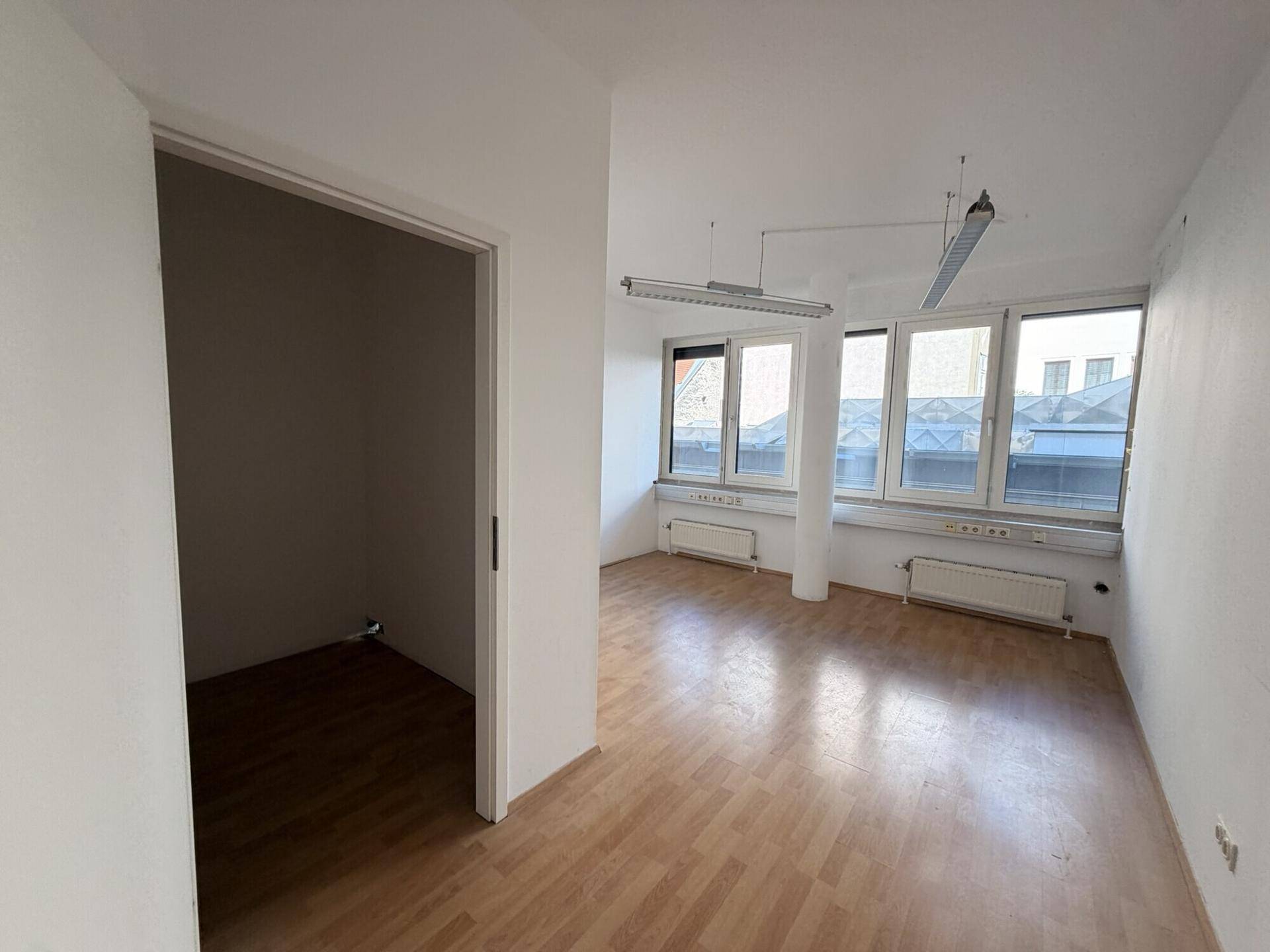 Helles Büro mit Laminatboden und Zugang zu einem kleineren Nebenraum.
