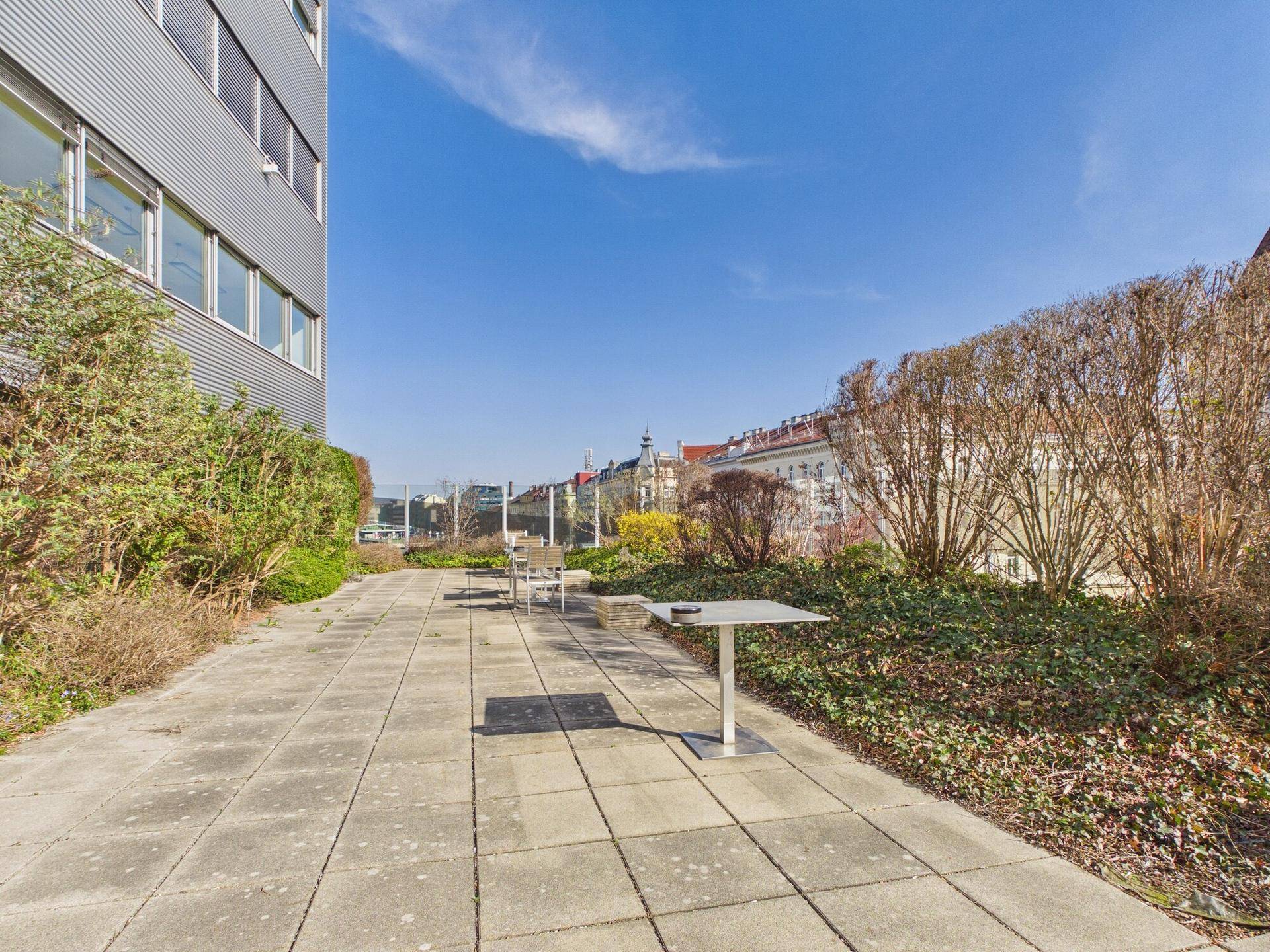 Grüne Dachterrasse mit Sitzgelegenheiten und Blick auf die umliegende Stadtbebauung.