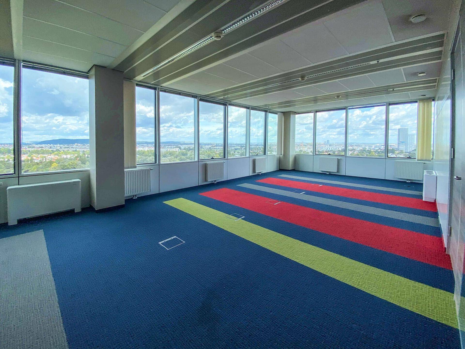 Helles Büro mit Teppichboden in verschiedenen Farben und Panoramablick auf die Stadt.