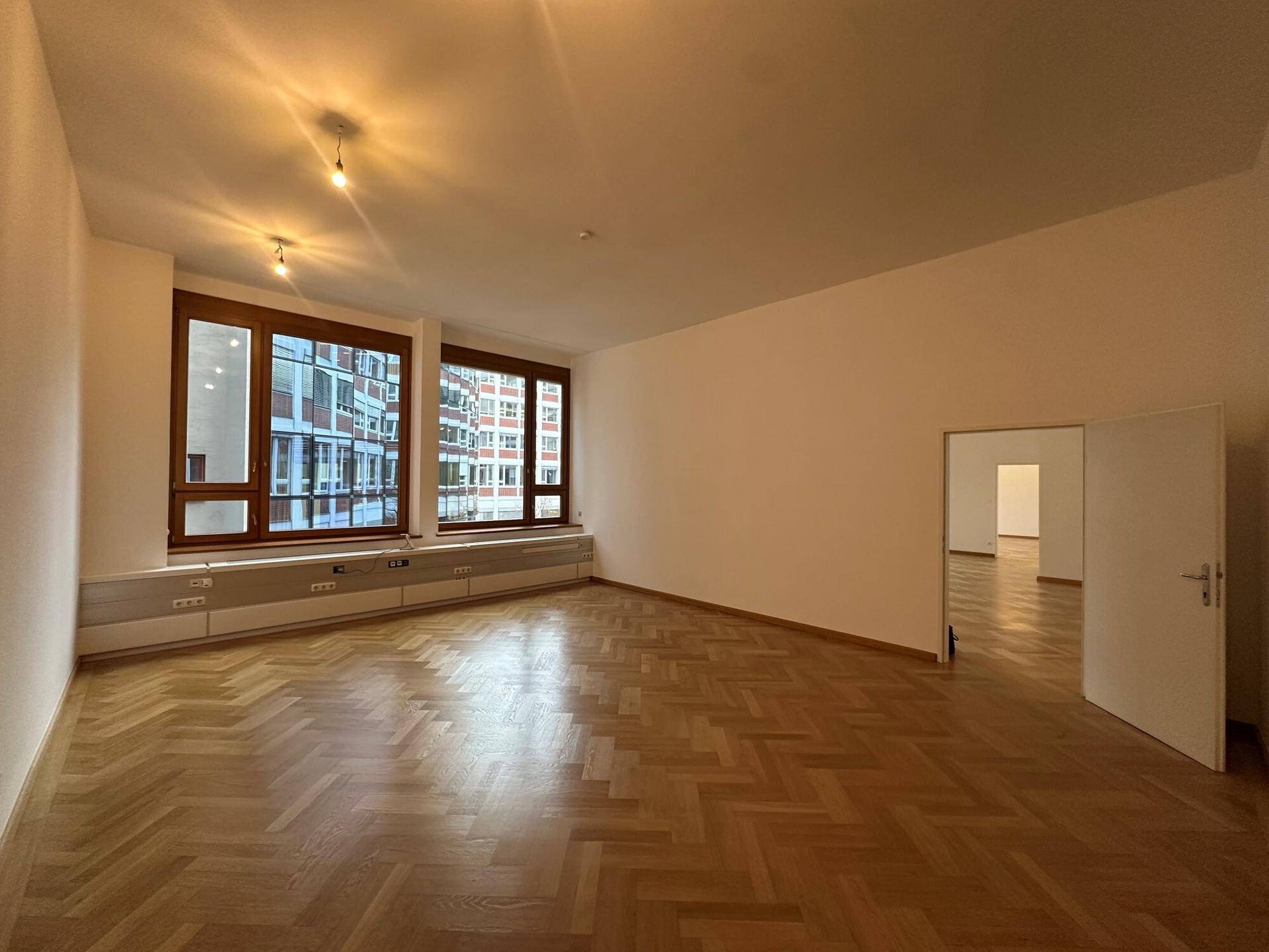 Heller Raum mit Fischgrätparkett und großen Fenstern, die einen Blick auf die Umgebung bieten.
