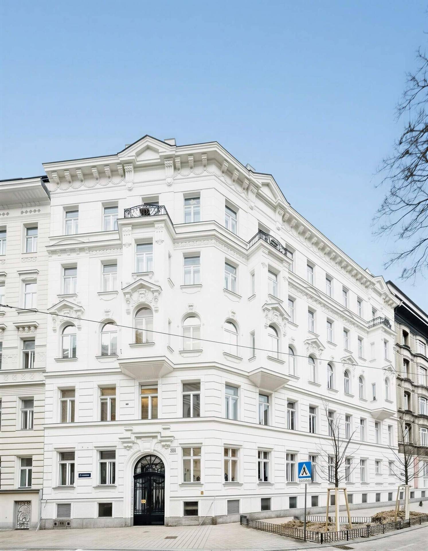 Prächtiges weißes Altbaugebäude mit klassischer Architektur, vielen Fenstern und kleinen Balkonen unter blauem Himmel.