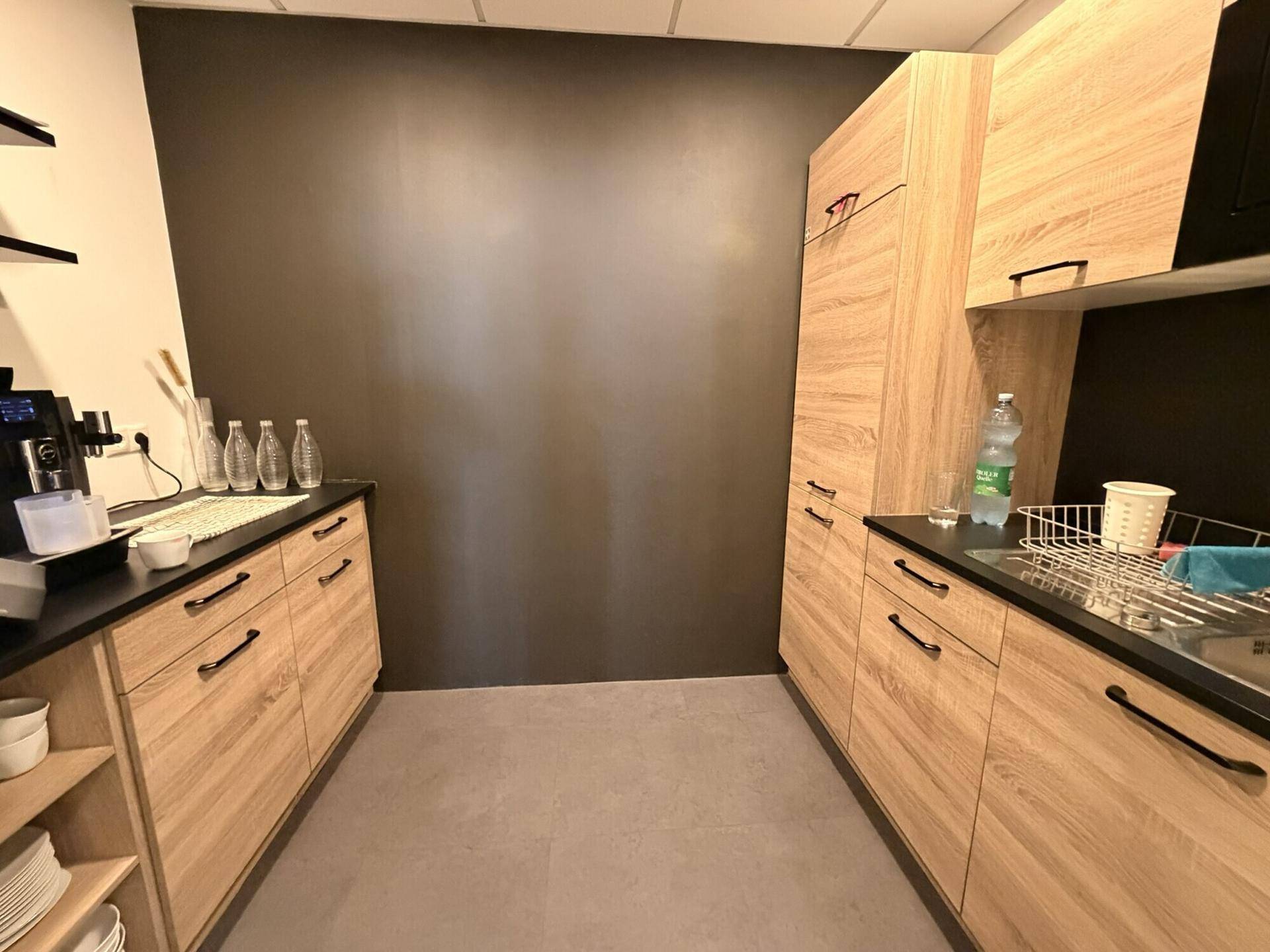 Kleine Küchenzeile mit Holzschränken, dunkler Arbeitsplatte und Kaffeemaschine, ideal für Pausen.