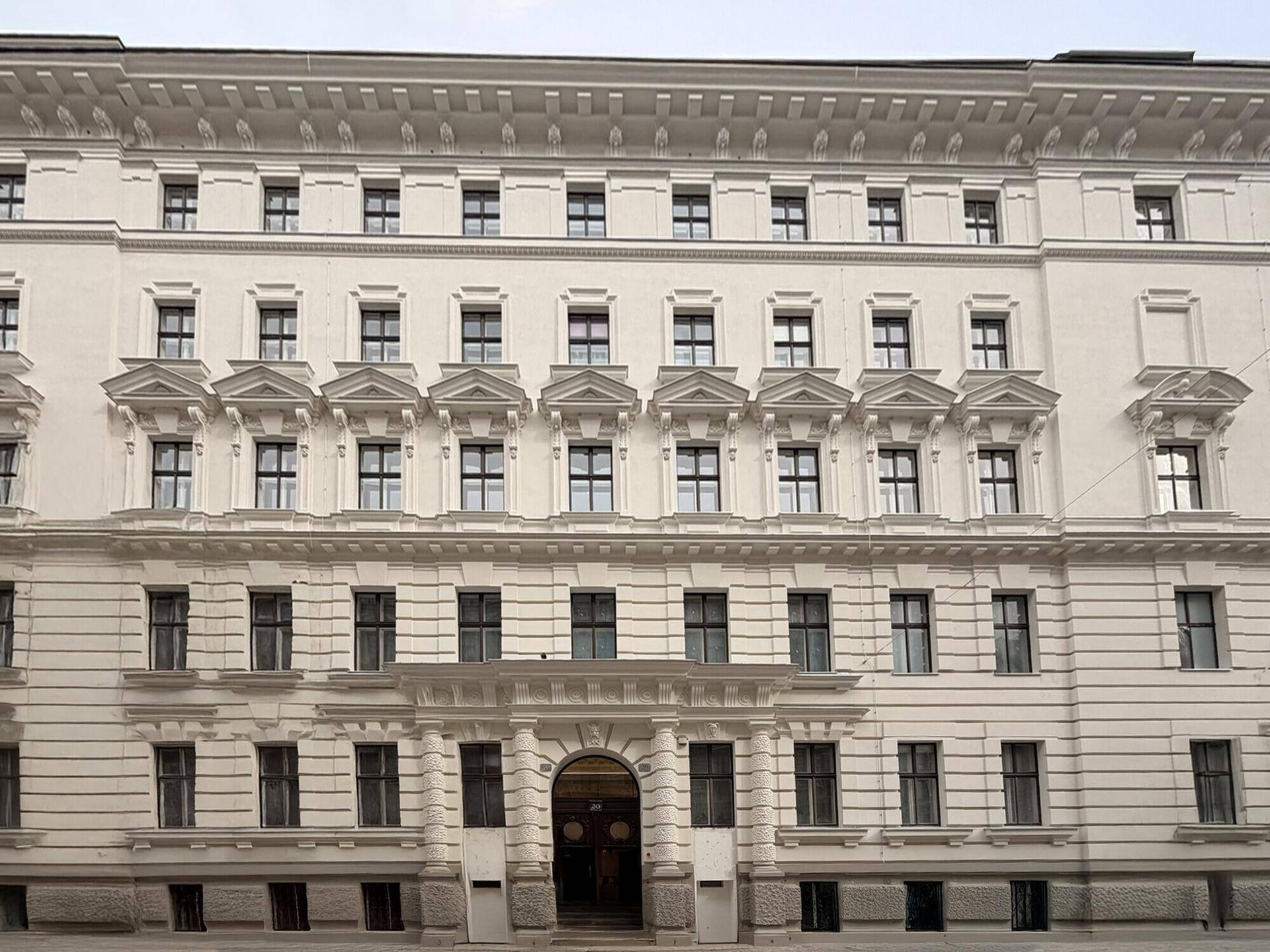 Klassische, weiße Fassade eines historischen Gebäudes mit vielen Fenstern und dekorativen Elementen.