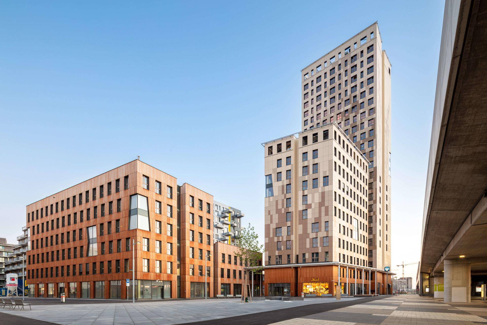Moderne Gebäude mit Holzfassaden und großen Fenstern in einer städtischen Umgebung bei klarem Himmel.