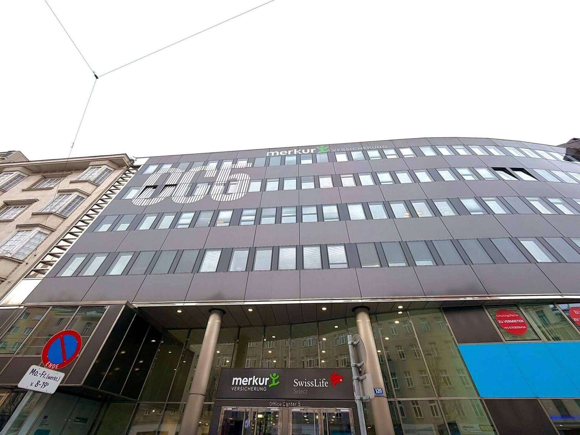 Moderne Bürogebäude-Fassade mit vielen Fenstern und Firmenbeschriftungen unter bewölktem Himmel.